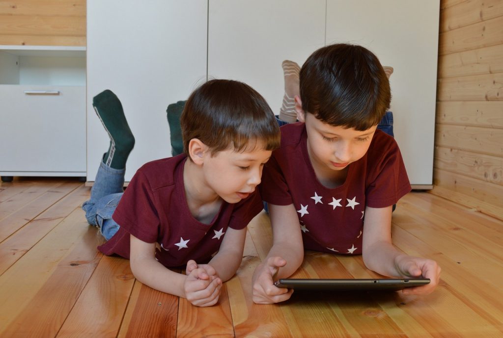 Two boys laying on the floor playing with a tablet device.