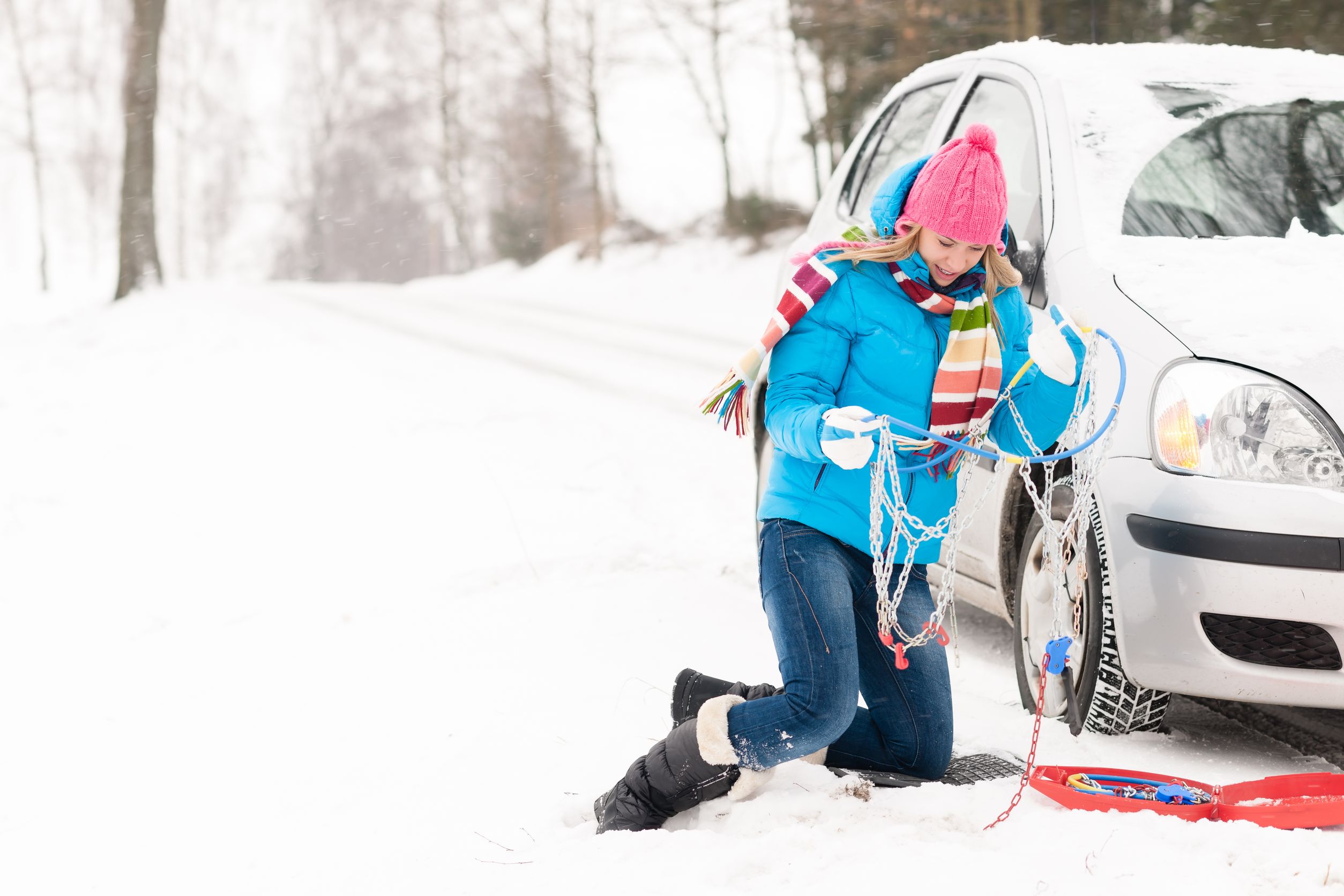 woman with tire chains next to car in snow breakdown needing exhaust fitting