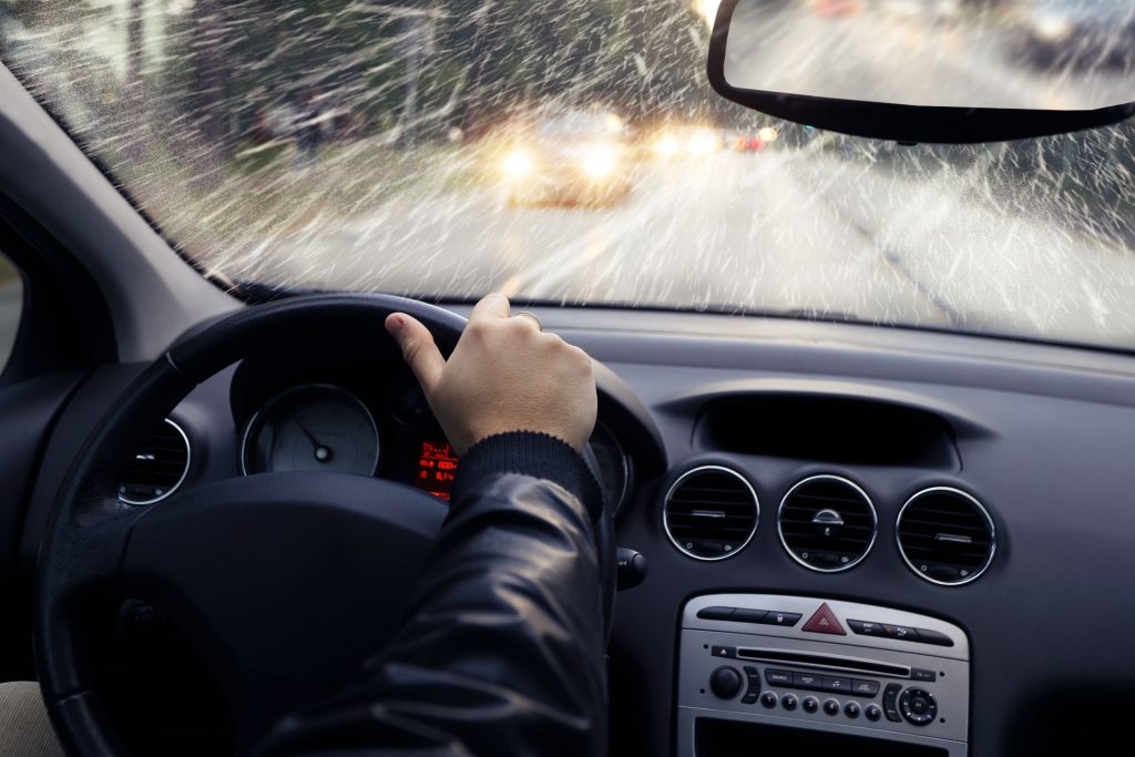 adult hands holding steering wheel in a car on a snowy road to discuss options for exhaust fitting services.