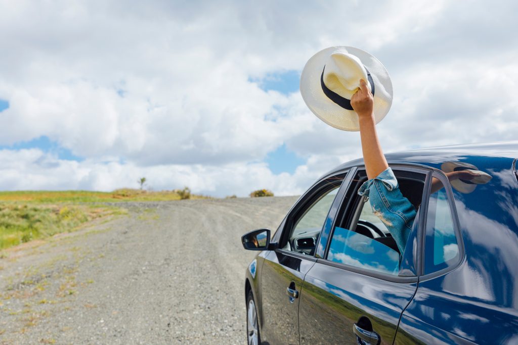 A hand holding a hat hanging out of the car to express joy.
